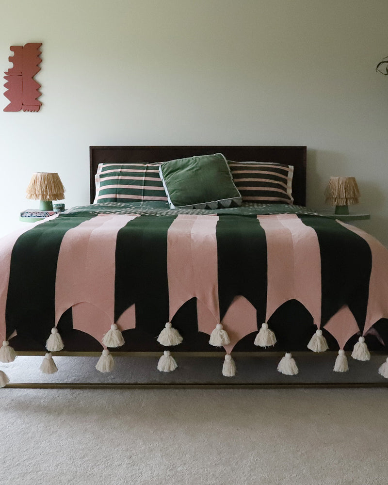Bed with green and pink striped blanket with tassels in a bedroom setting.