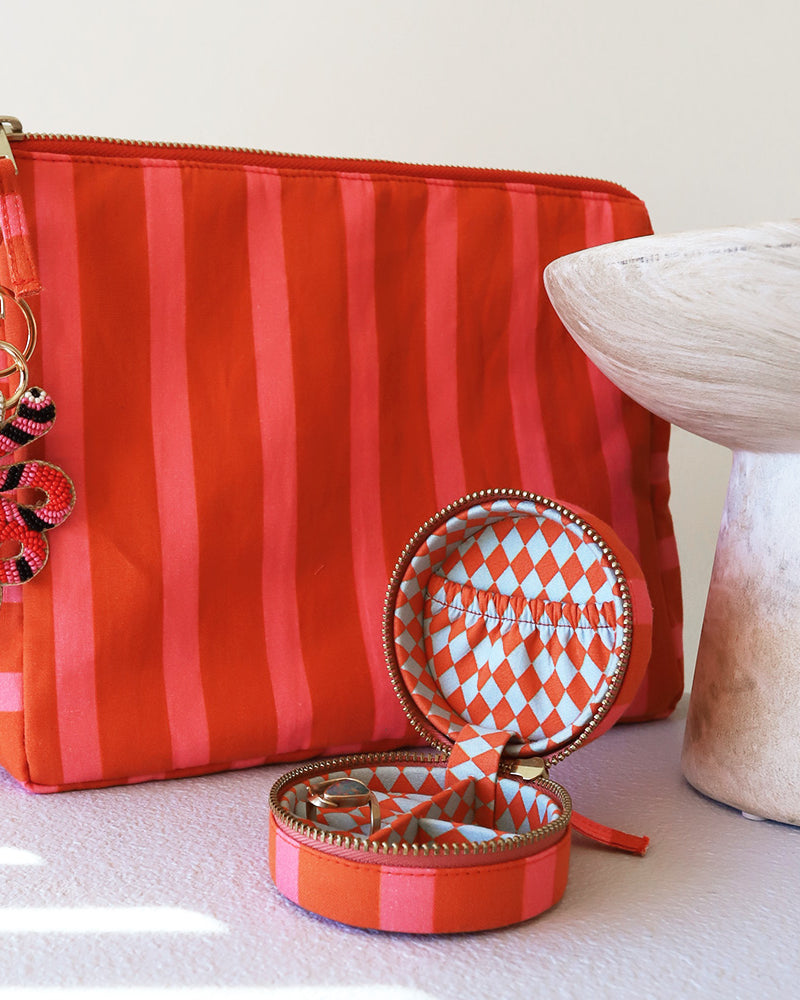 Orange and pink striped cosmetic pouch with beaded charm and matching jewellery case on a white surface