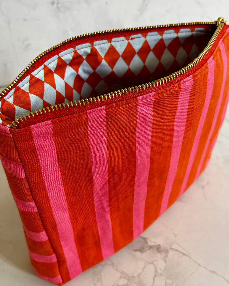 Red and pink striped pouch with gold zipper on a light marble background