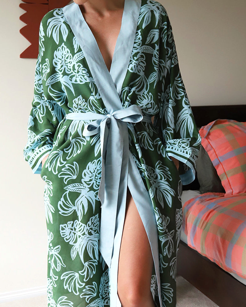 Person wearing a green monstera leaf floral robe in a bedroom setting