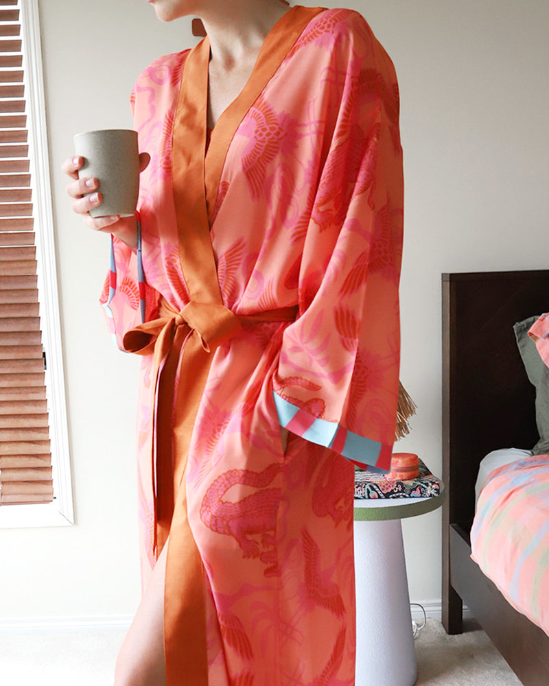 Person wearing a pink and orange summer robe holding a mug in a bedroom setting.