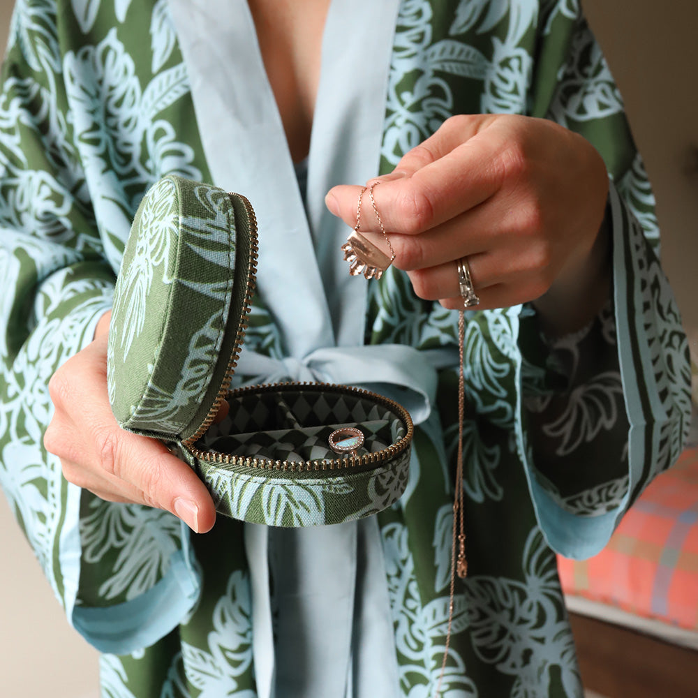 Person holding a green jewellery case with jewelry, wearing a patterned robe.