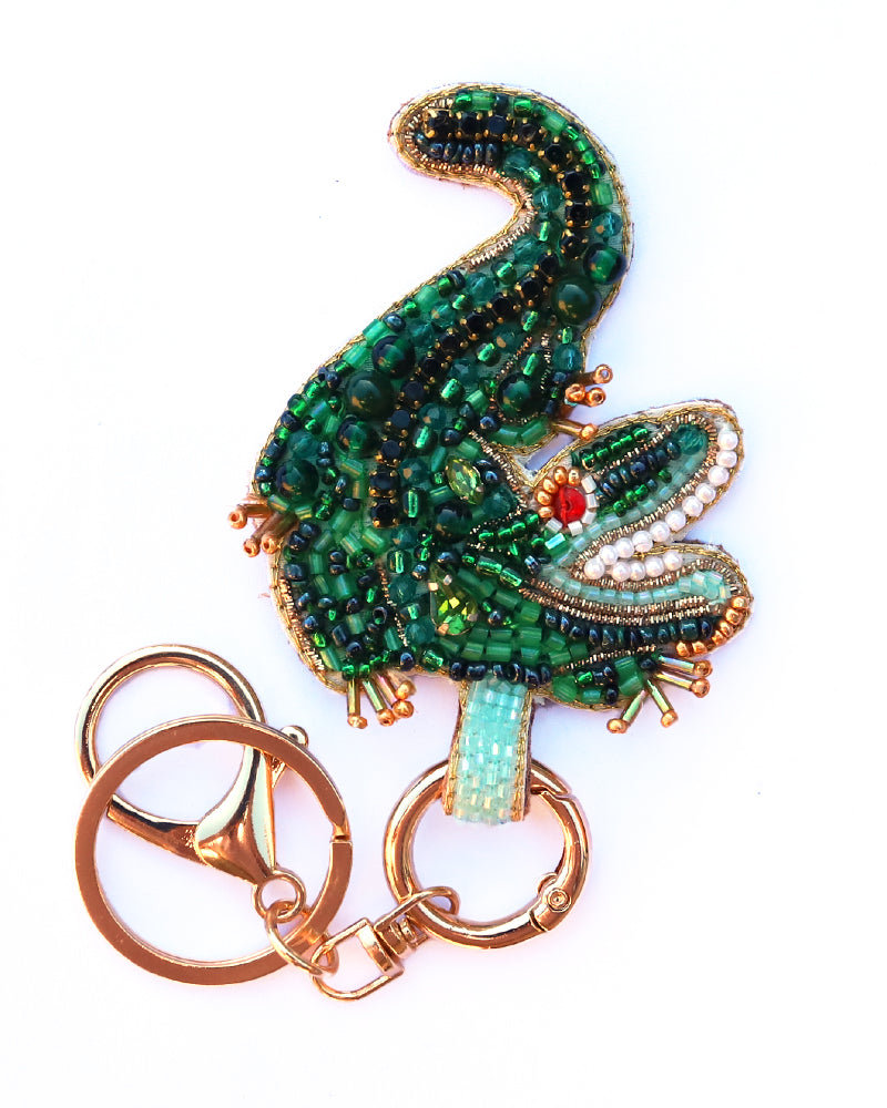 Decorative crocodile keychain with green beaded design on a white background