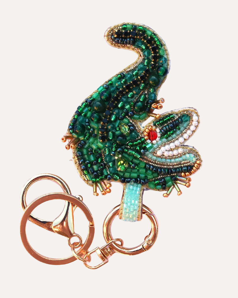 Decorative crocodile keychain with green beaded design on a white background