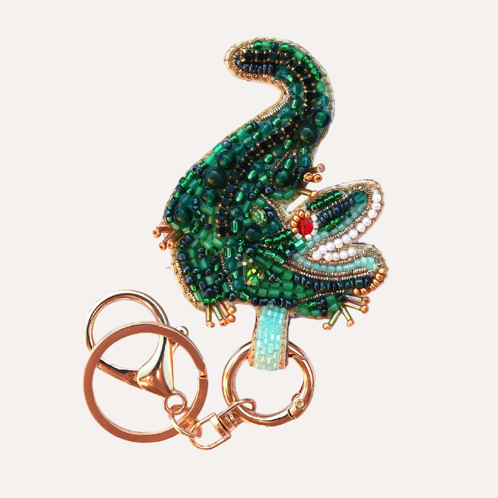 Decorative crocodile keychain with green beaded design on a white background