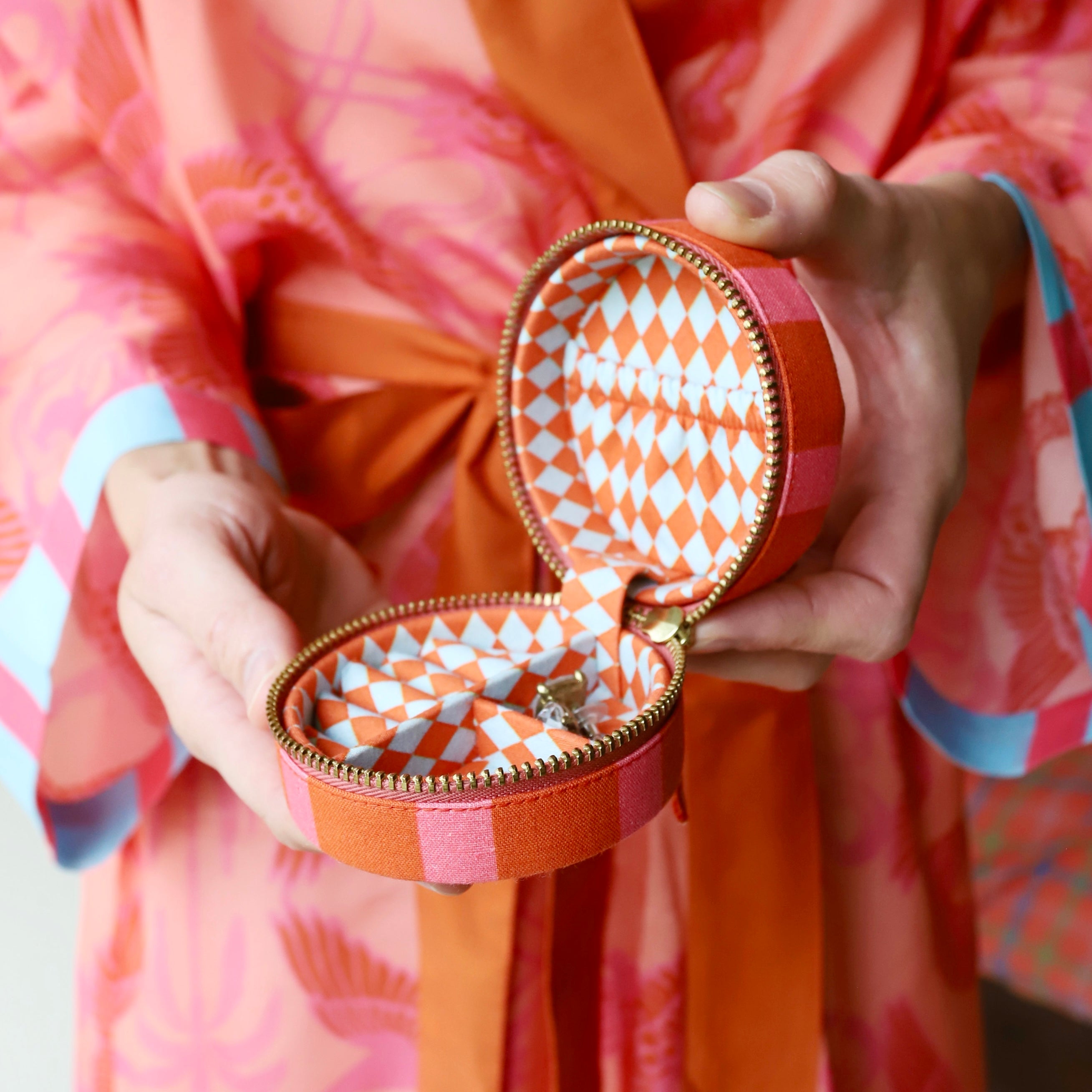 Person holding an open orange jewelry box with geometric pattern, wearing a colorful robe garment.