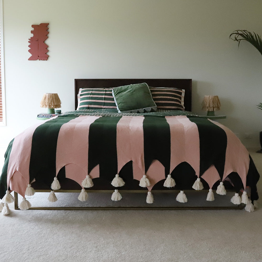 Bed with green and pink striped blanket with tassels  in a bedroom setting.