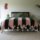 Bed with green and pink striped blanket with tassels  in a bedroom setting.