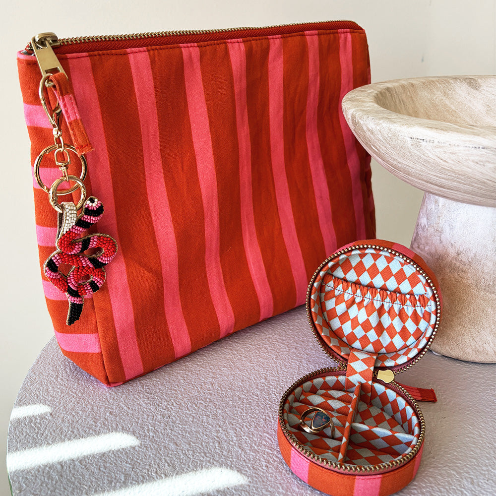 Orange and pink striped cosmetic pouch with beaded charm and matching mini jewellery box on a white surface