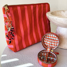 Orange and pink striped cosmetic pouch with beaded charm and matching mini jewellery box on a white surface