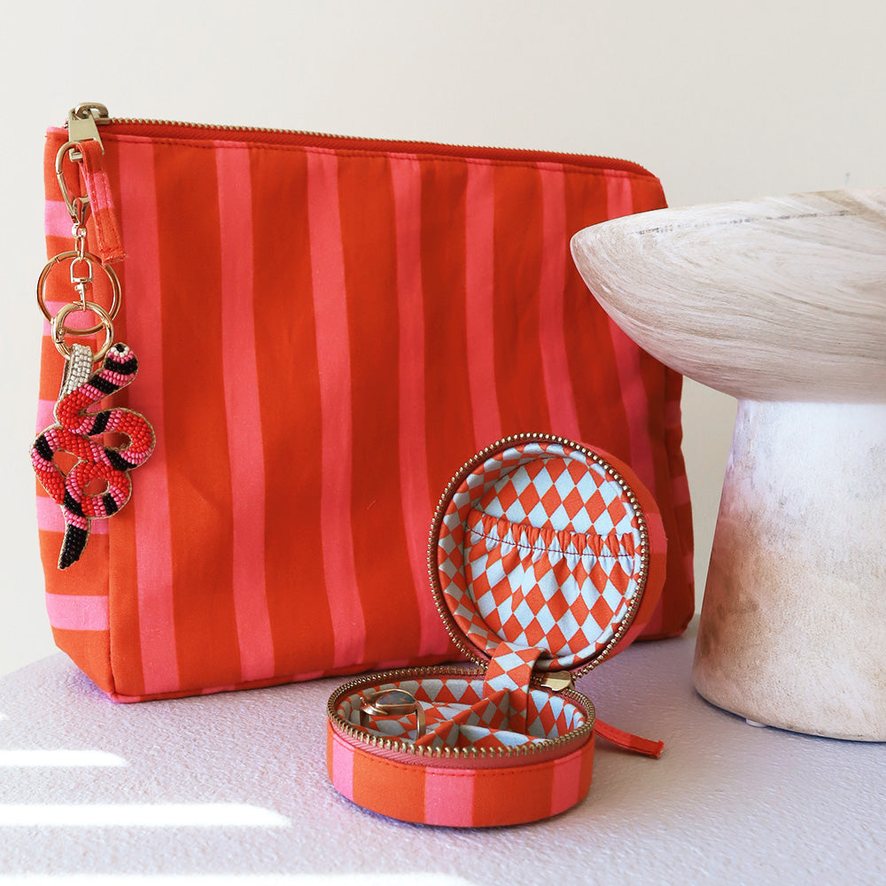 Orange and pink striped cosmetic pouch with beaded charm and matching jewellery case on a white surface