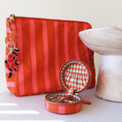 Orange and pink striped cosmetic pouch with beaded charm and matching jewellery case on a white surface