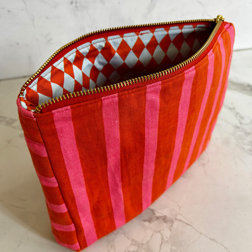 Red and pink striped pouch with gold zipper on a light marble background