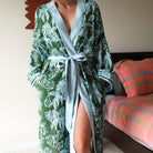 Person wearing a green monstera leaf floral robe in a bedroom setting