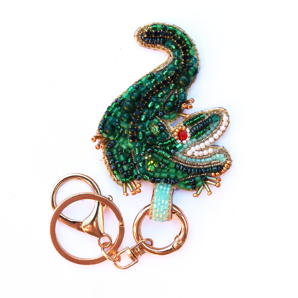 Decorative crocodile keychain with green beaded design on a white background